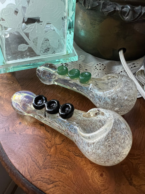 Two Ripkitty 4" silver fumed frit glass hand pipes side by side — one with green jade marble accents, one with black rose marble accents — displayed on a wood surface